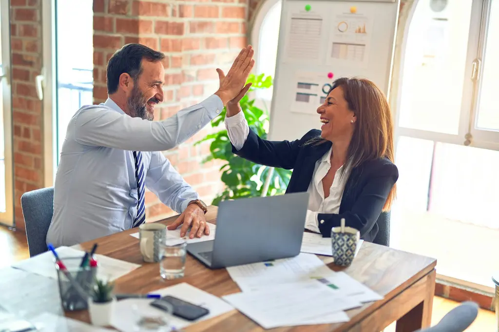 Two colleagues celebrating a successful meeting at a desk with a laptop
