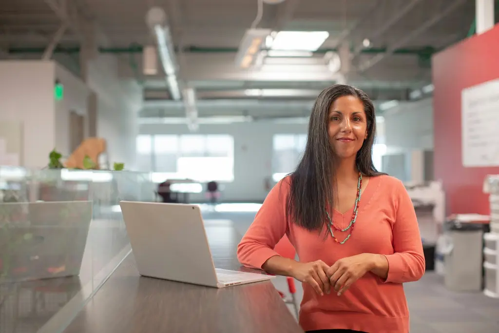 A smiling professional standing at a desk with a laptop in a modern office