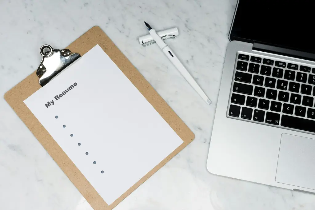 A clipboard with a blank CV template next to a laptop and pen