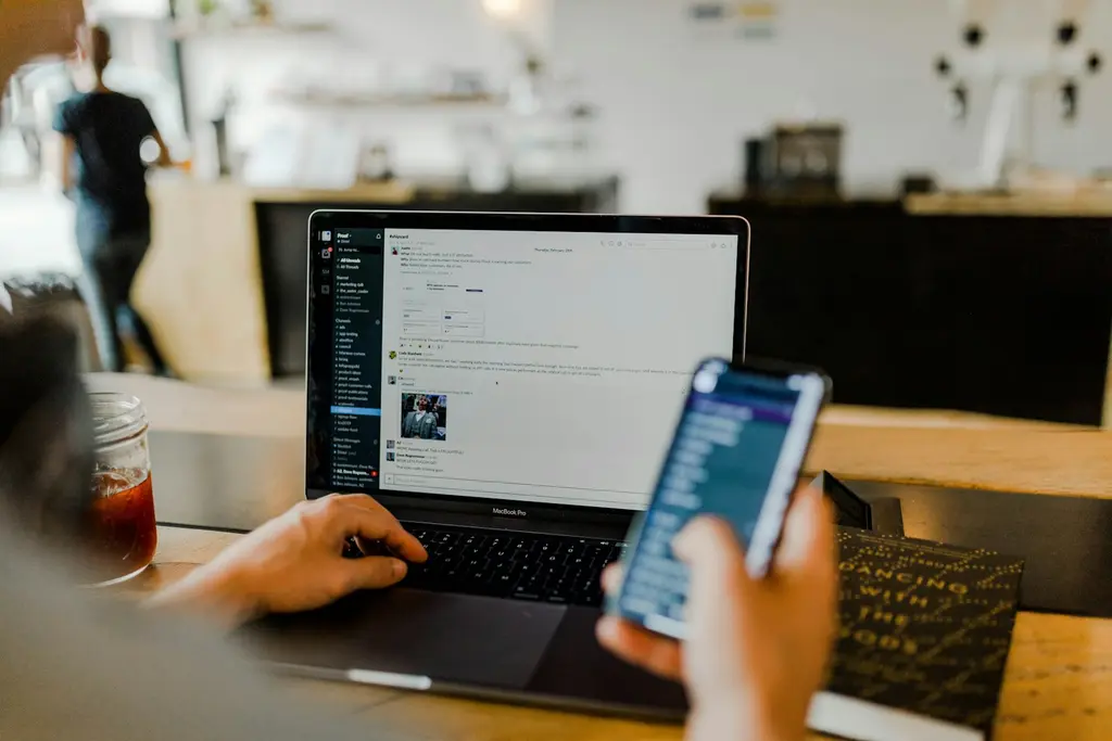 A person using a laptop and a mobile phone at a desk