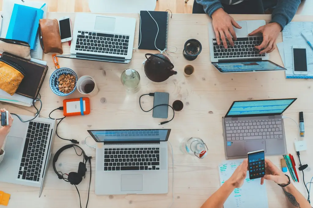 An overhead view of colleagues working on several laptops around a wooden table