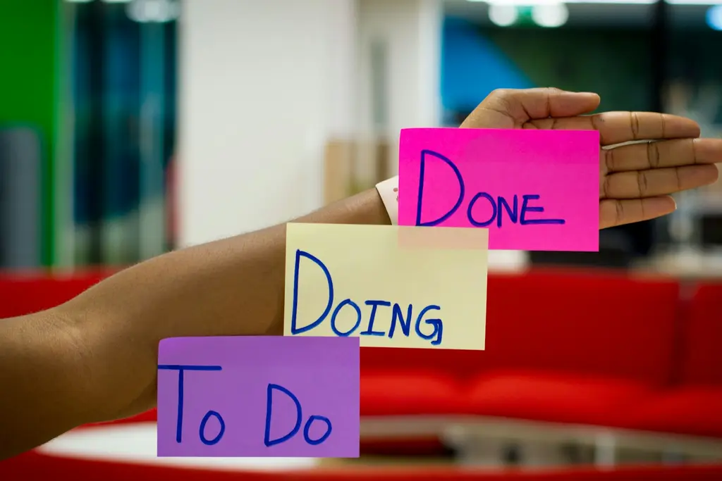 Hands holding sticky notes labelled To Do, Doing and Done